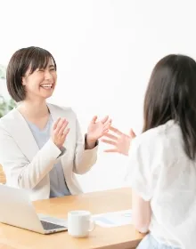 テーブルで向かい合いながら会話をする女性たち。笑顔で楽しくコミュニケーションを取っている様子。