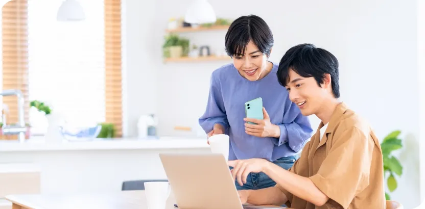 アジア人カップルがキッチンでノートパソコンとスマートフォンを使っている様子。