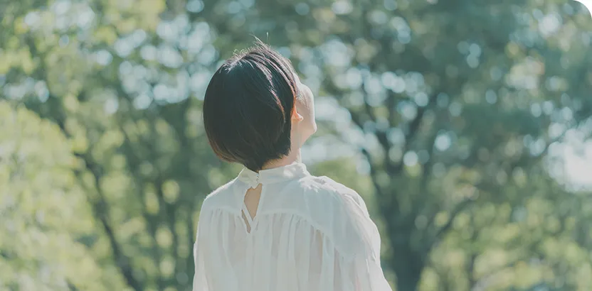 白いドレスを着た女性が木々を見上げている後ろ姿の画像。