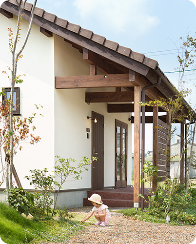 小さな子供が家の前で地面に座っている様子を描写した画像の代替テキストです。